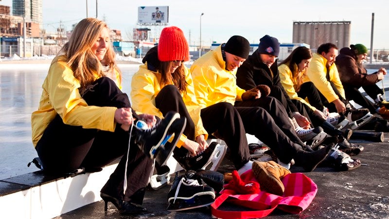 group of people sitting on an edge and lacing up their ice skates.