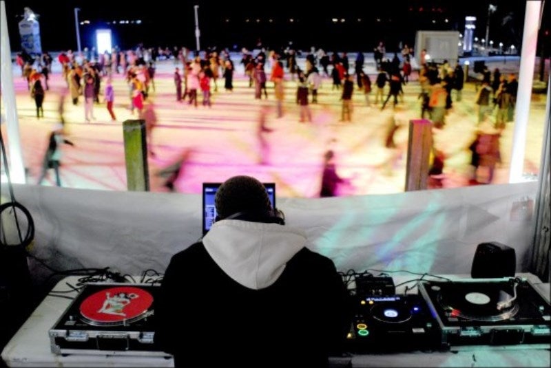 A DJ in his booth looking out at a busy outdoor ice rink at night.