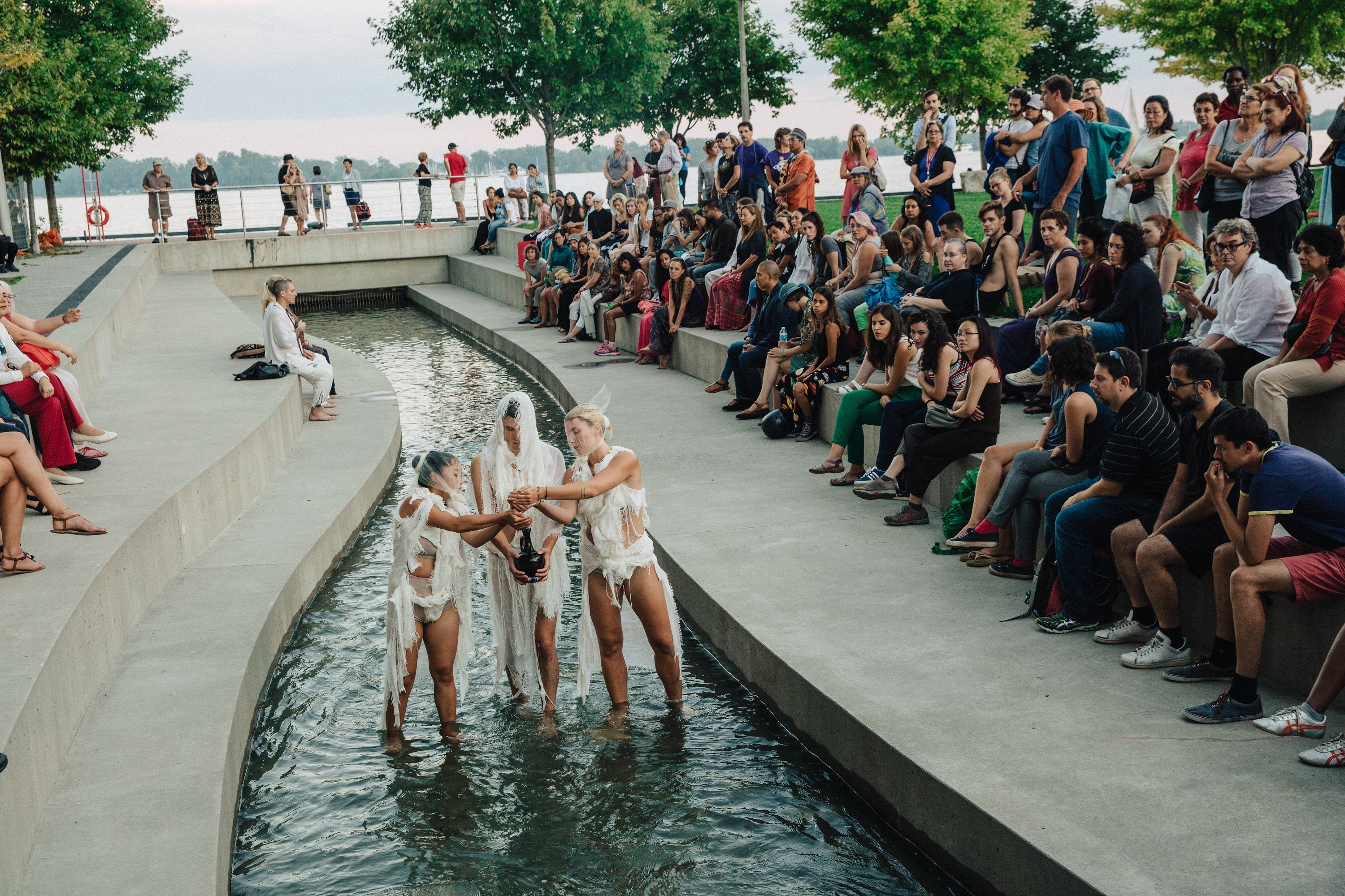 An audience watching The Gata: Water Ceremony performers in the urban river at Sherbourne Common.
