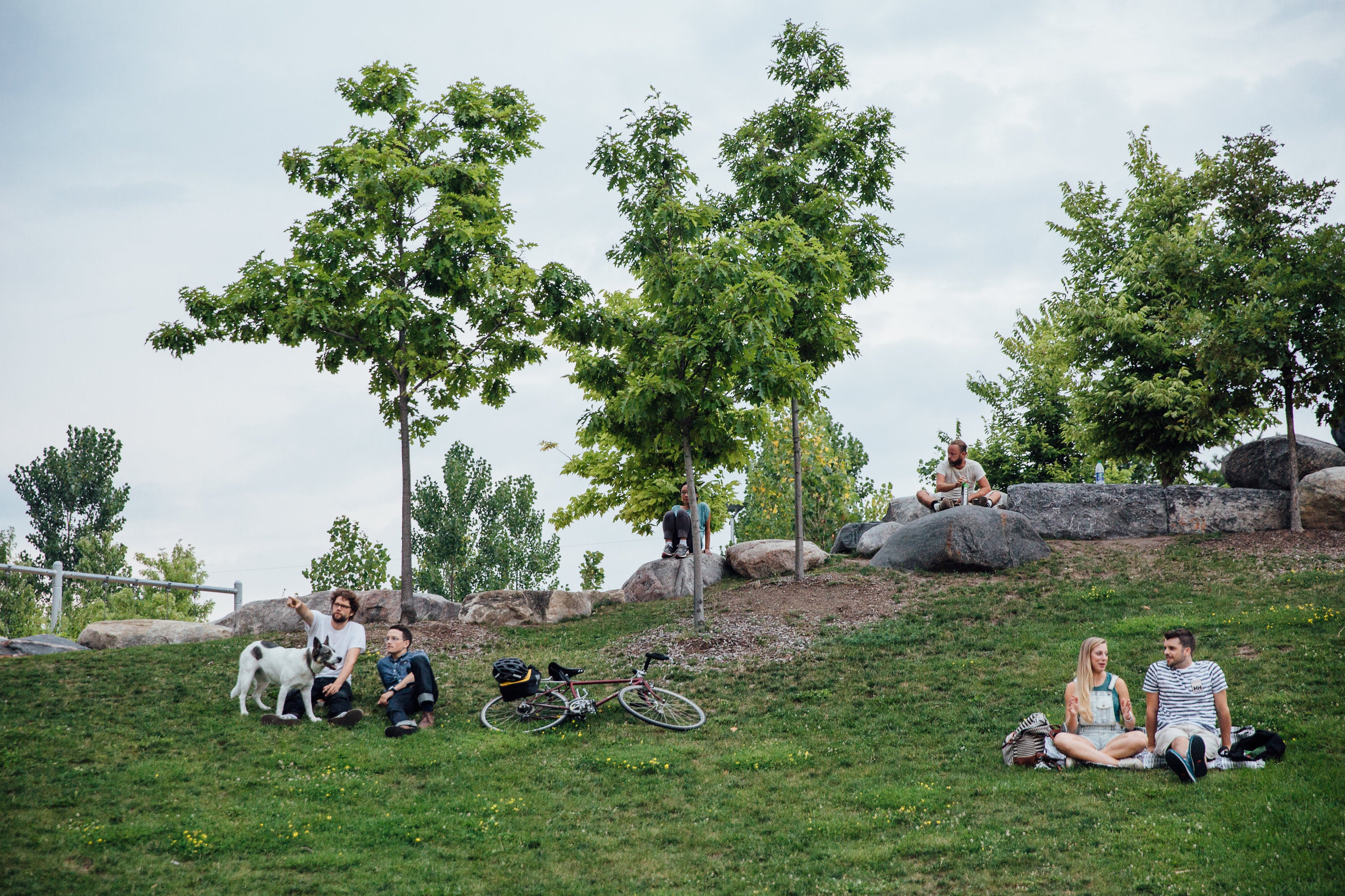 Park-goers sitting on the gently sloping hill of the south lawn at Corktown Common.