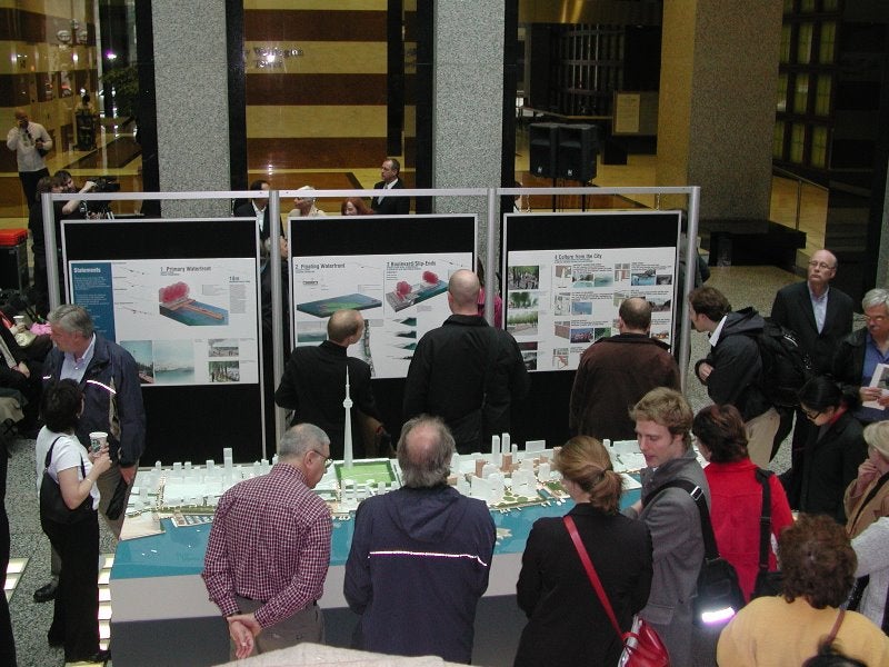 People gathered around display boards and a large design model.