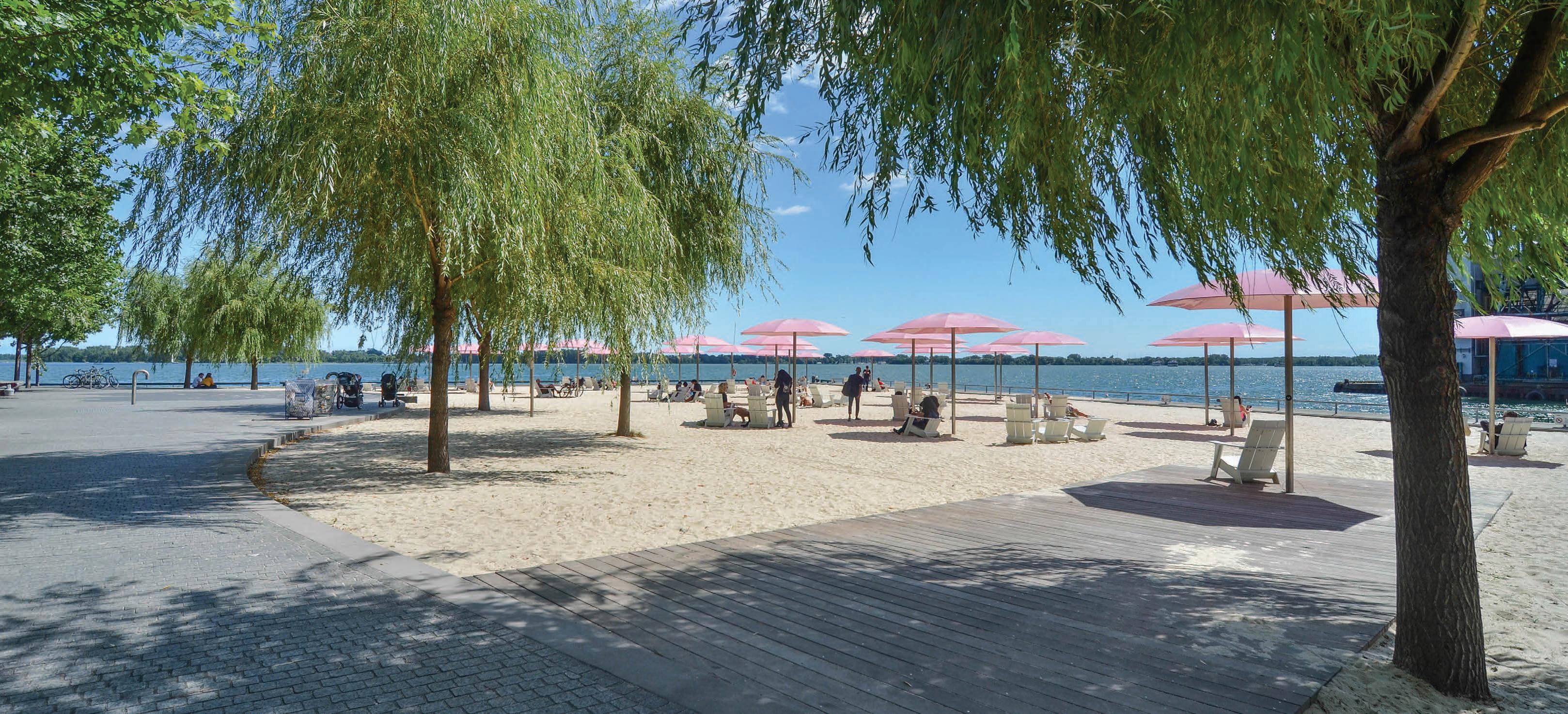 a sandy urban beach with pink umbrellas and trees