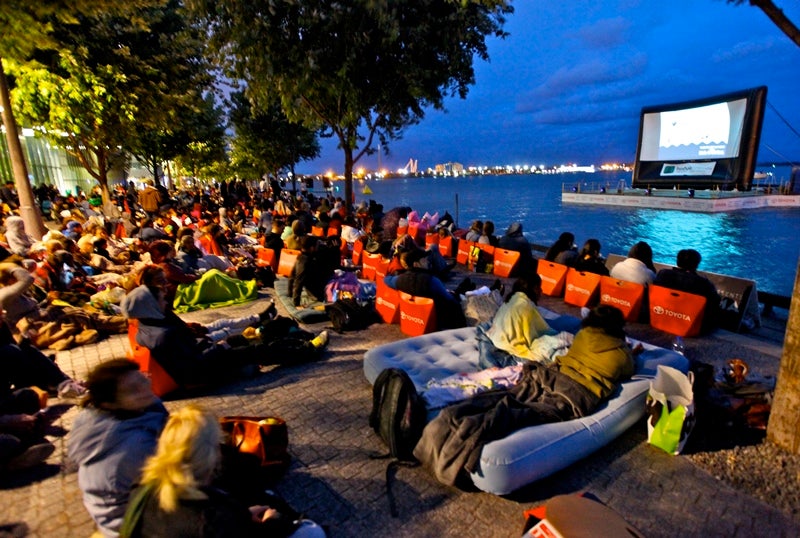 a busy water's edge promenade with an outdoor movie at night