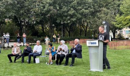 A person speaks at a podium next to people sitting in a park