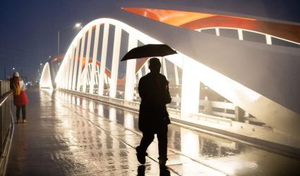 A person walking across a new bridge in the rain and at dusk