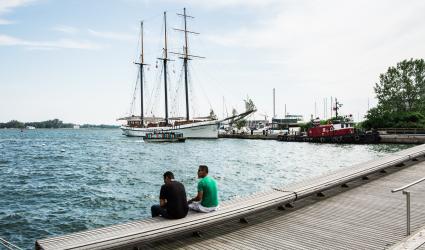 Two people sitting on a long wooden bench next to the lake.