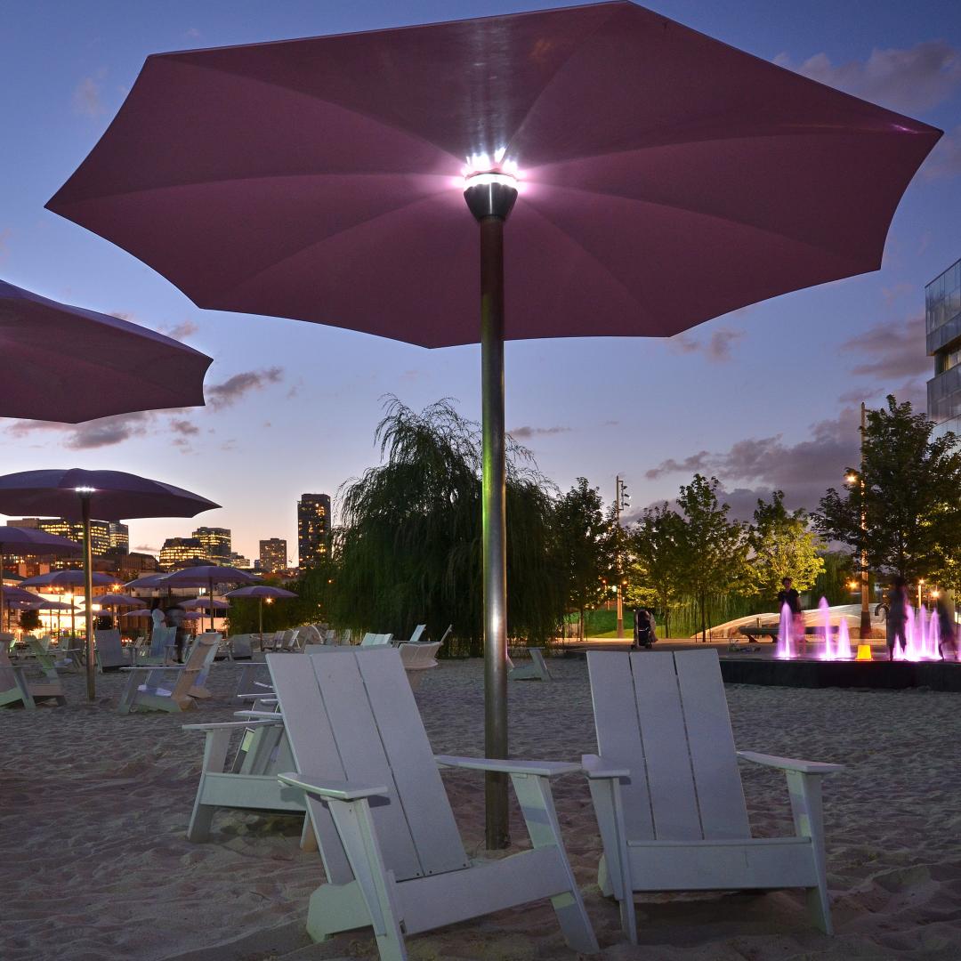 showing pink umbrellas, white Muskoka chairs and sandy beach lit up at dusk