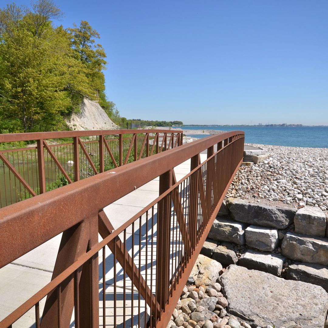 a pedestrian bridge next to the cobblestone beach and Lake Ontario