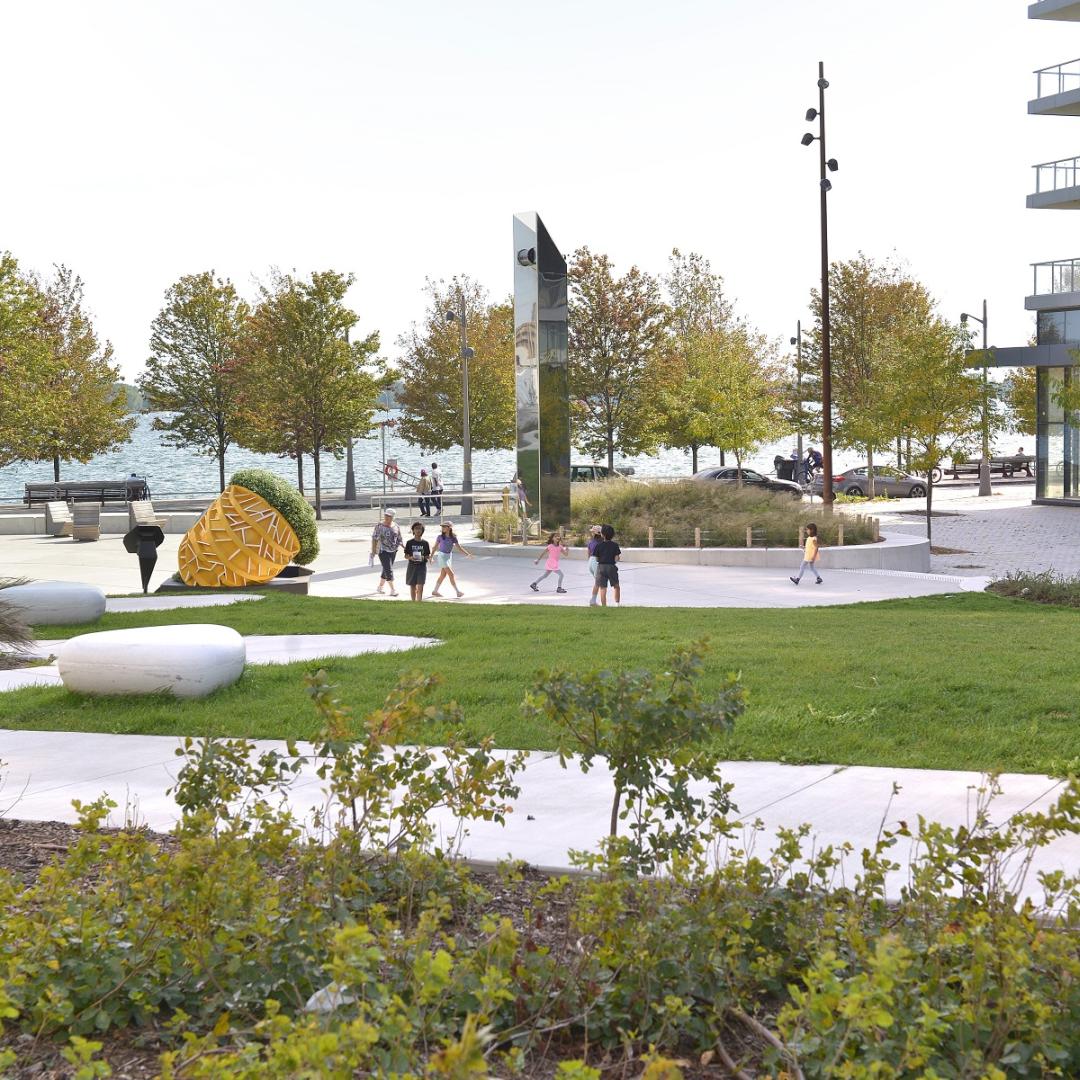 a group of children in a park next to a public art piece and the water's edge