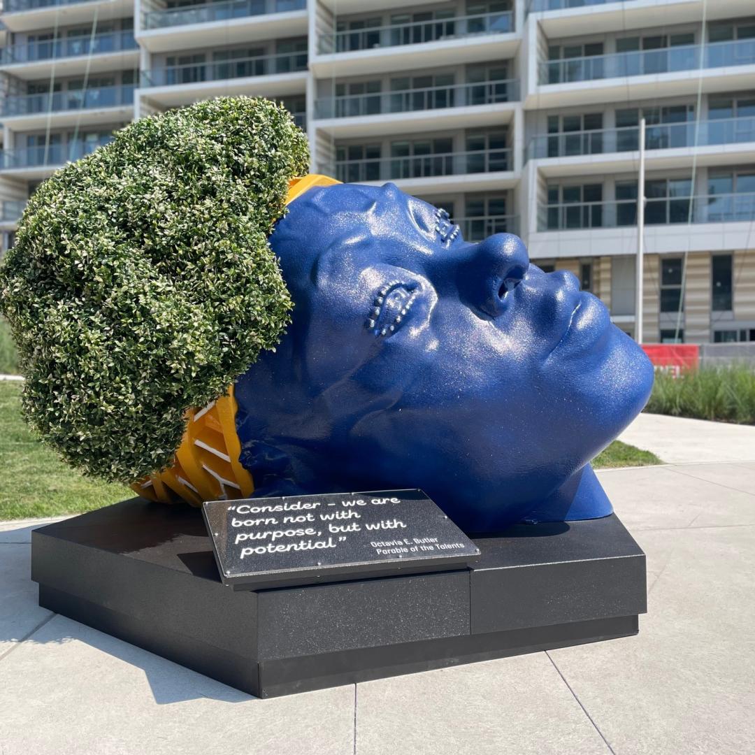 a striking temporary public art installation of a large blue head with grass for hair