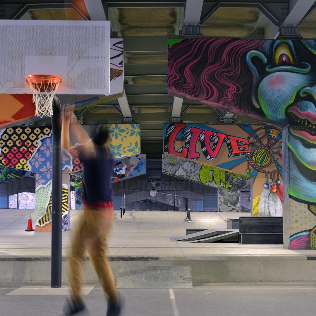 a person playing basketball in an outdoor underpass park next to graffit pillars