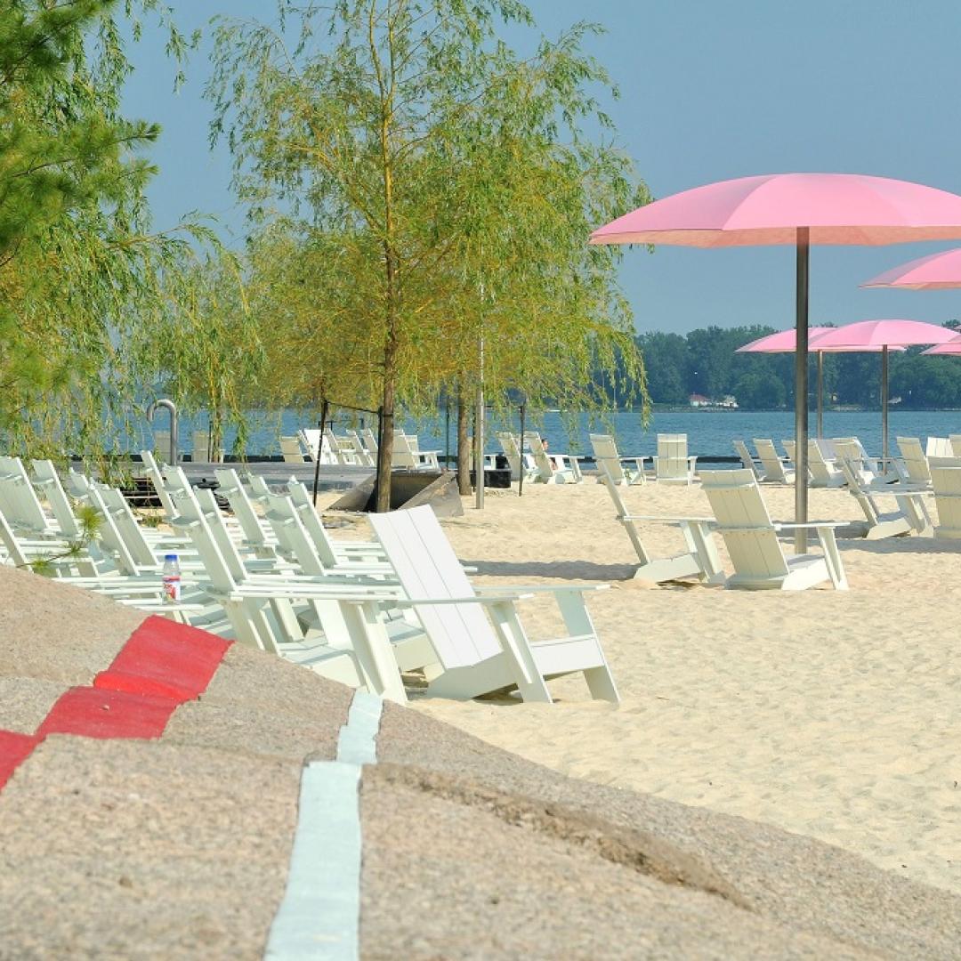 an urban waterfront beach with pink umbrellas, colourful striped rocks for seating, and a sandy beach