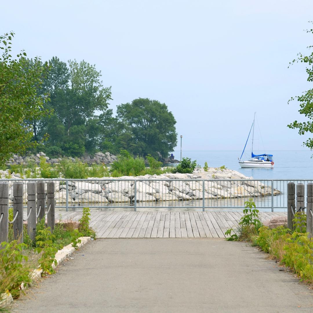 a waterfront trail and path leading to the lake with a sail boat in the background