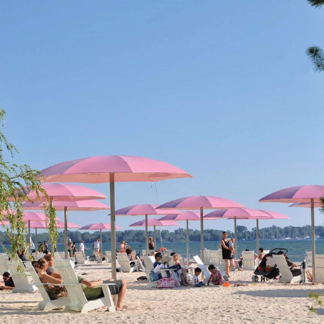 A crowded beach on a summer day. People sitting under pink umbrellas. 