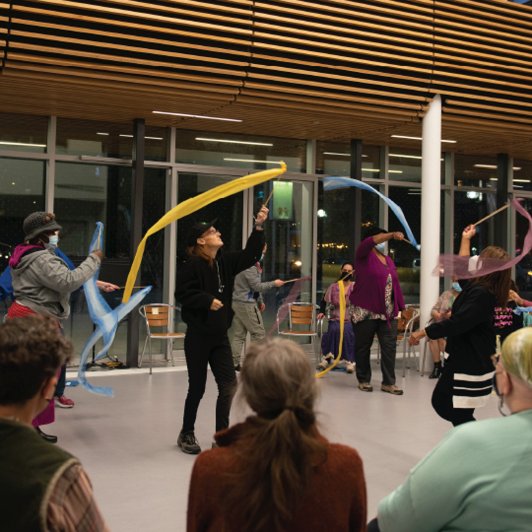 people gathered around watching an outdoor performance with ribbons