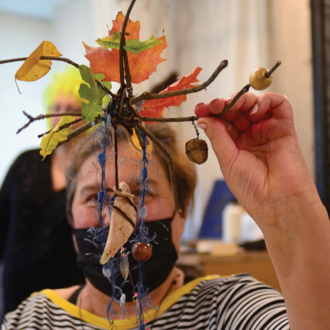 a woman holding a piece of art made from branches and leaves in front of her face