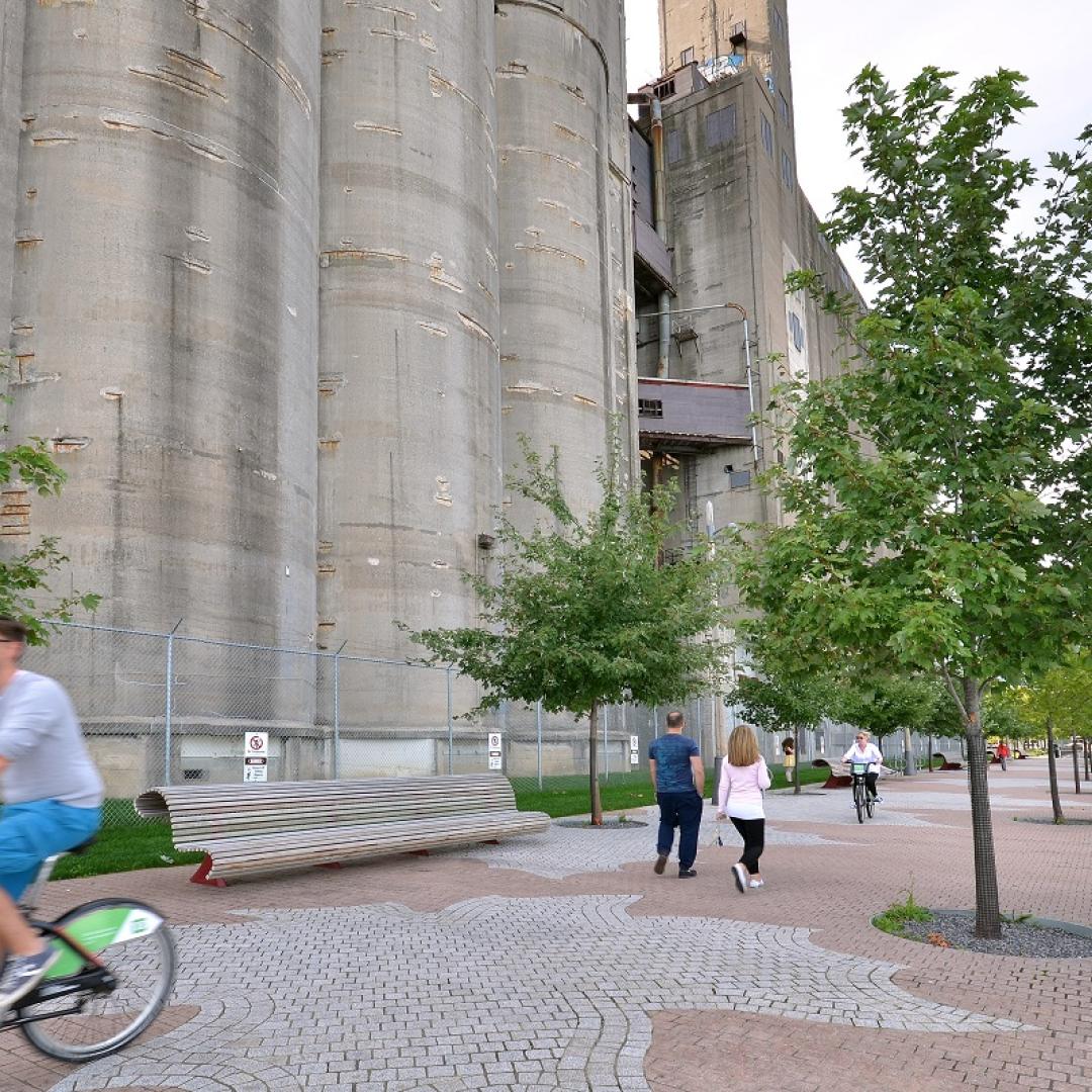 people walking and cycling along a waterfront promenade next to a silo building