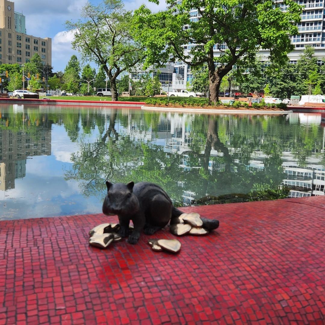 a bronze statue of a chipmunk sitting on a edge of a park's pond
