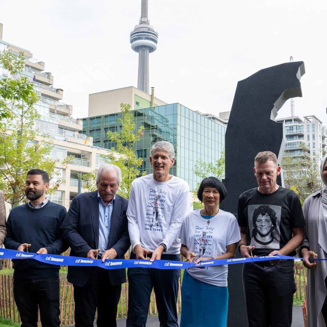 seven people cut a ribbon in front of a granite statue inspired by Terry Fox