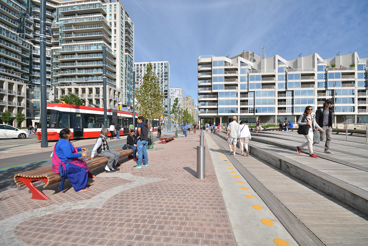 people sitting on a street bench next to an open public space and trail