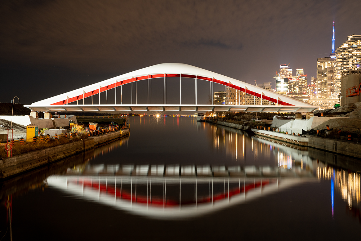 A red and white bridge with the city lit up at night in the background.