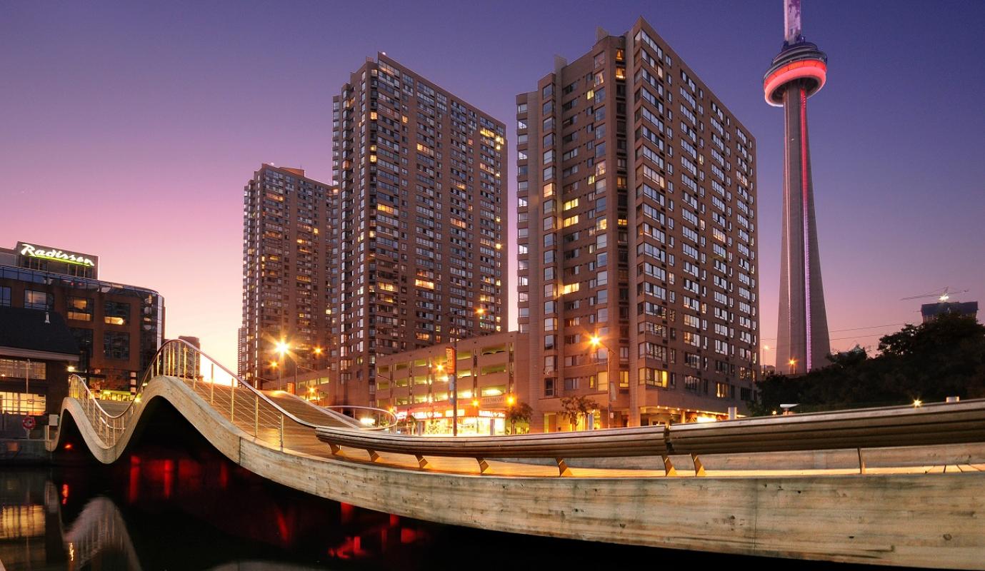 photo shows the curves and red underlighting of the Simcoe WaveDeck at dusk with buildings and the CN Tower in the background