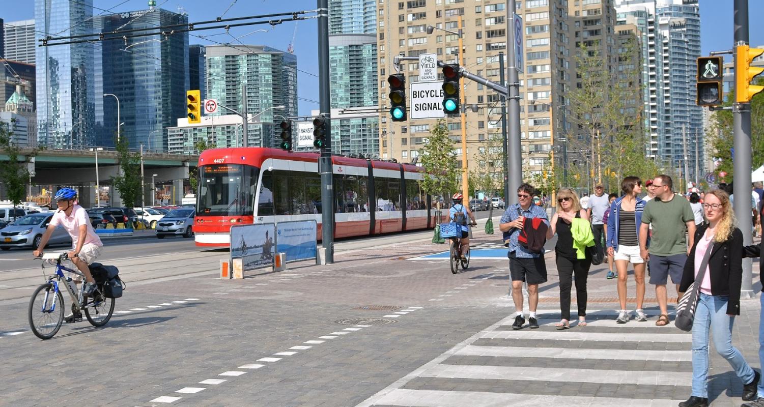 people walking along a busy street next to a multi-use trail and public transit