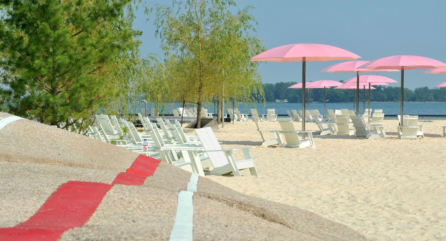 an urban waterfront beach with pink umbrellas, colourful striped rocks for seating, and a sandy beach