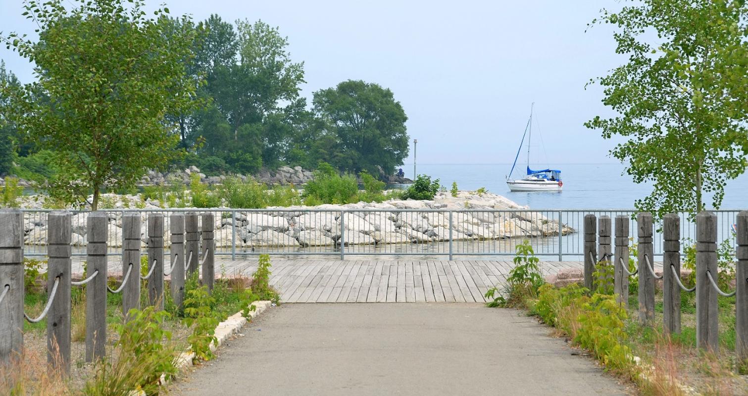 the shoreline and waterfront trail next to Lake Ontario with a sailboat in the background