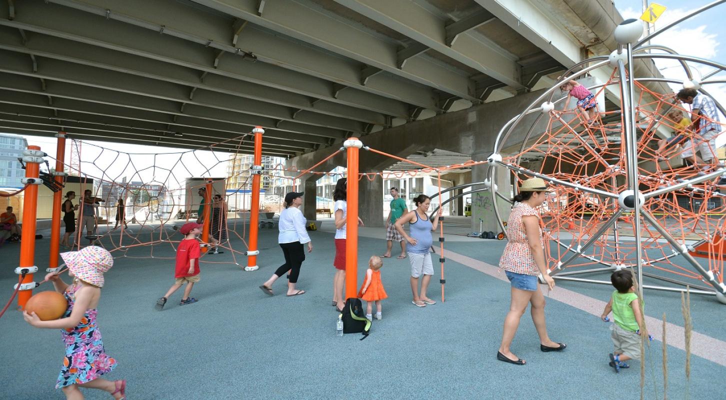 groups of families enjoying the play equipment at a new park underneath an underpass