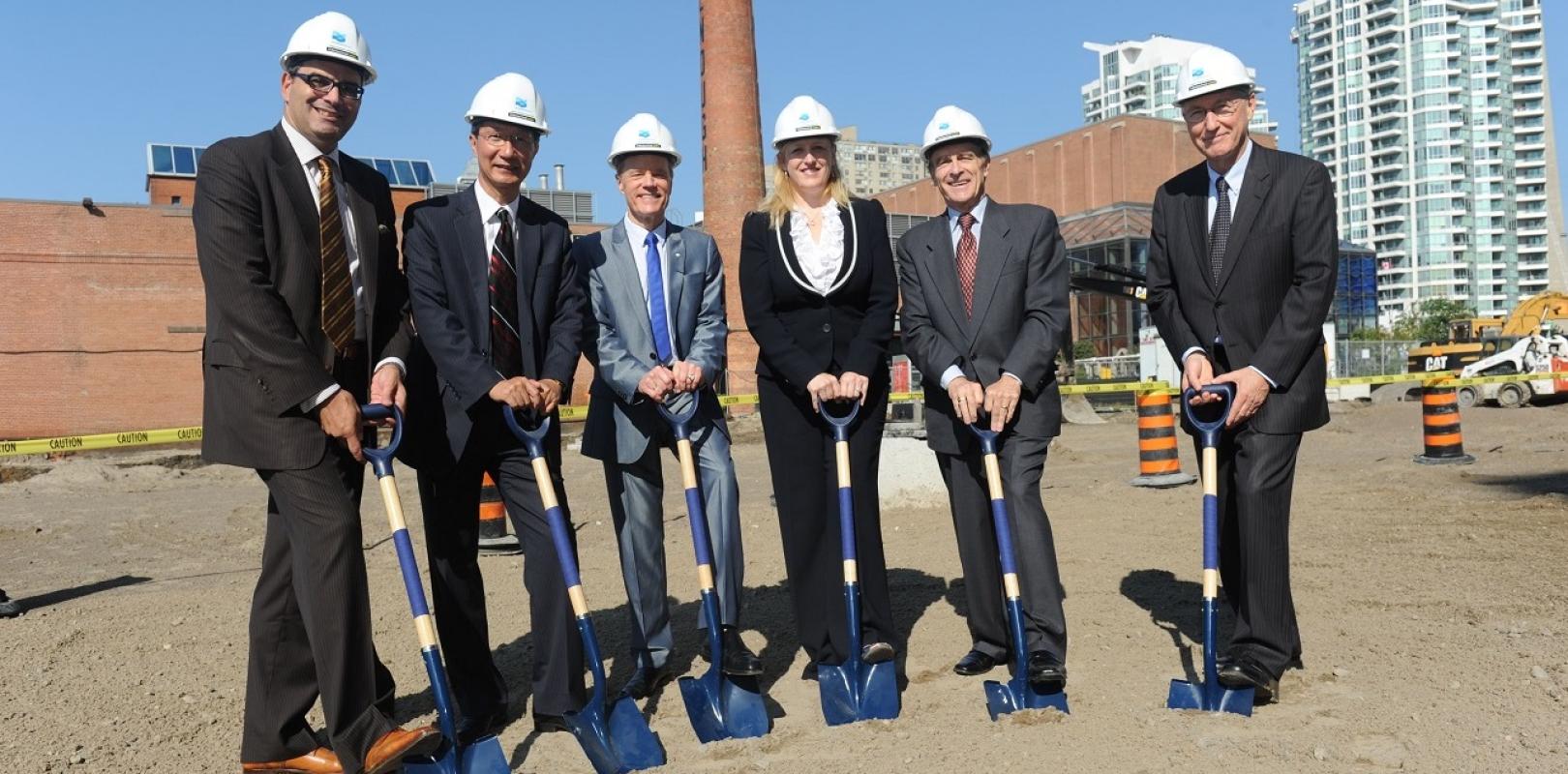 a group of people posing and wearing hard hats, holding shovels