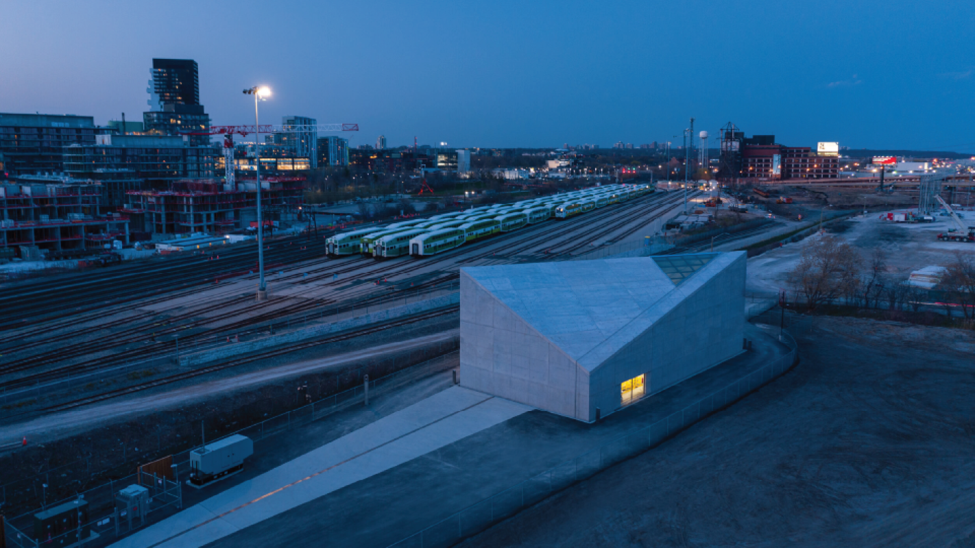 Aerial view of an angular building at dusk with a railyard in the background.