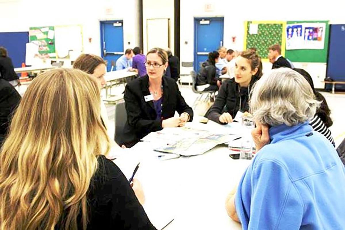 A group of people gather around a table and talk at a public meeting.