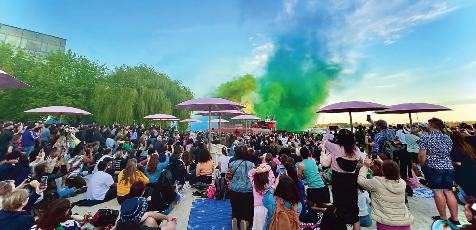 A crowd on a beach with a smoke sculpture in background.