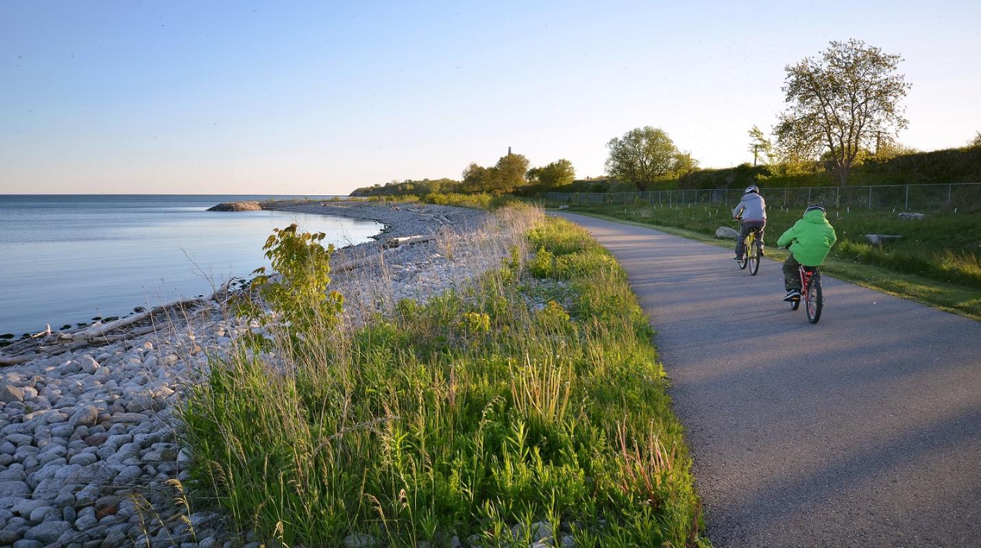 cyclists on a waterfront trail next to a cobblestone beach