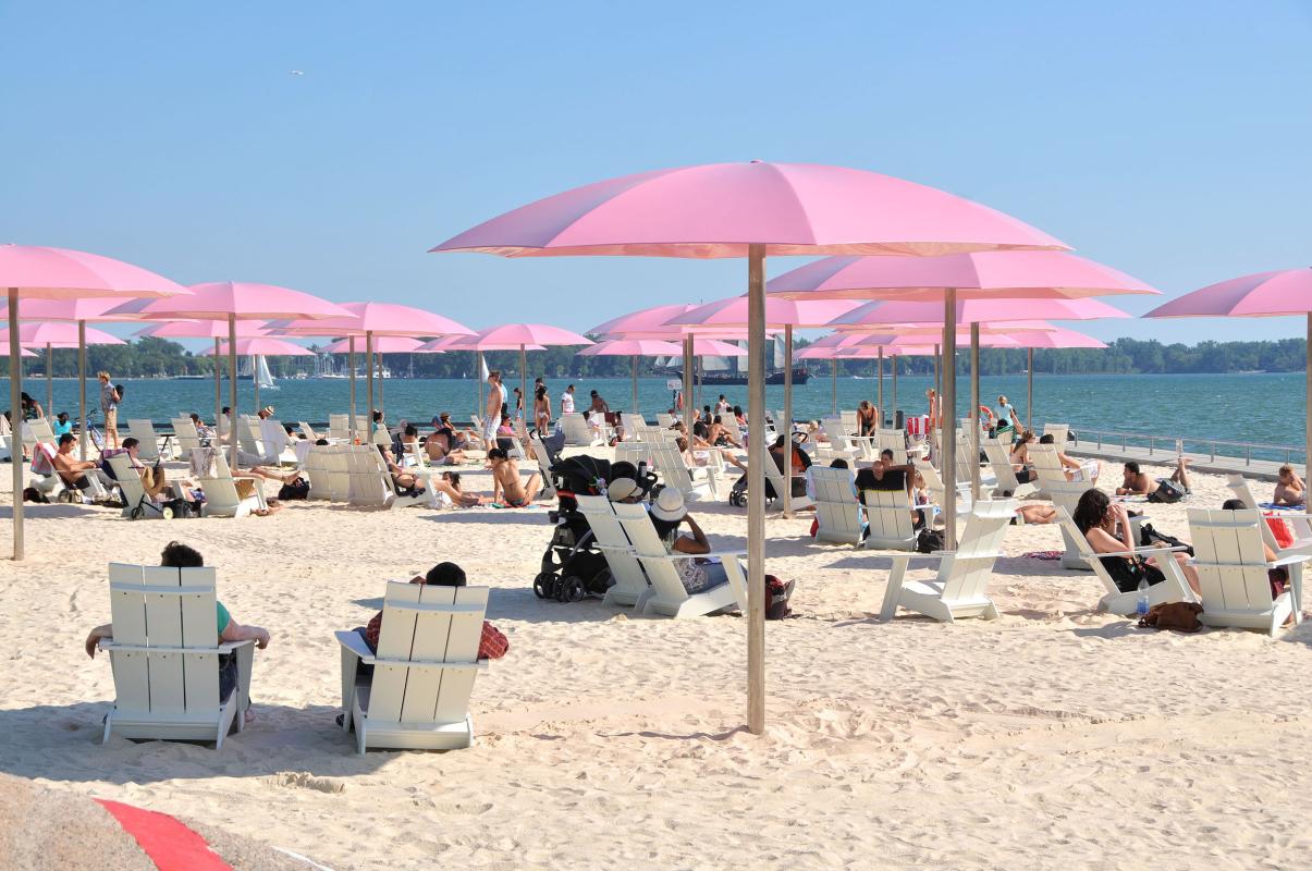 groups of people enjoying a sandy urban beach with pink umbrellas