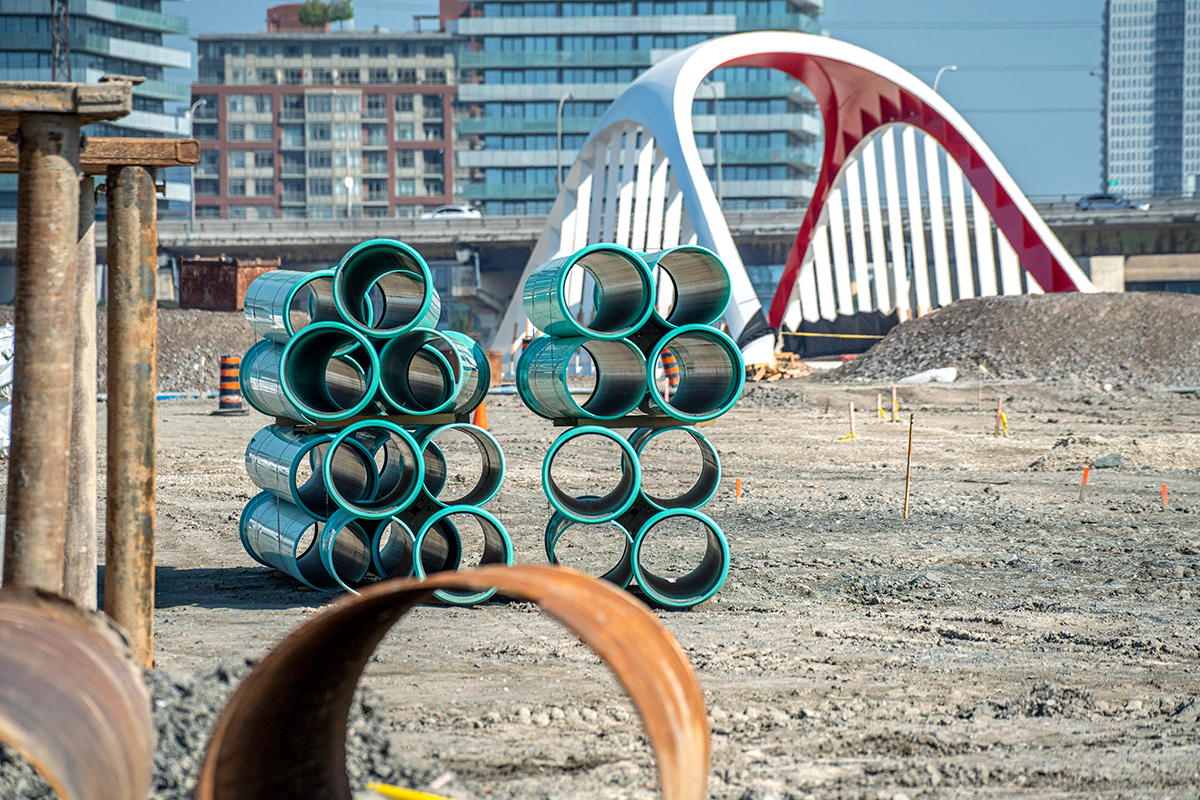 Blue pipes stacked in front of a bridge in a construction site.