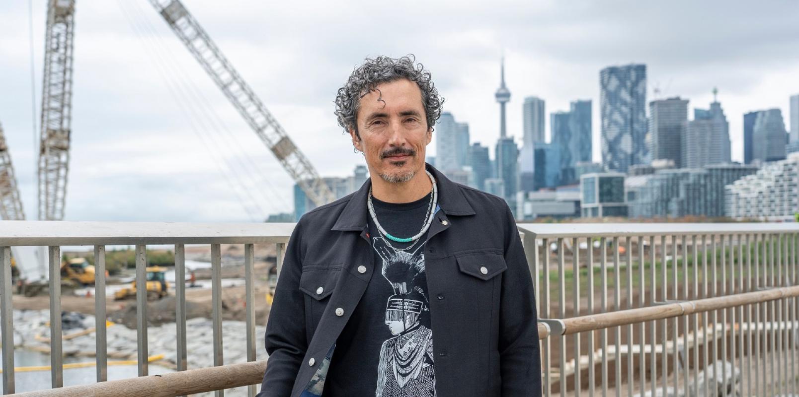 An individual dressed in black poses for the camera with Toronto's Skyline overlooking CN Tower in the backdrop.