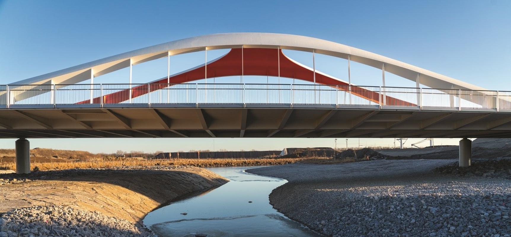 A modern bridge over a water body with concrete on the sides and sky in the background.