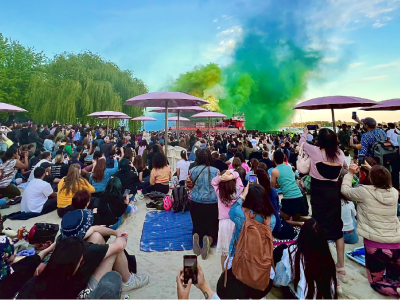 A crowd of people on a beach facing a green and blue smoke display.