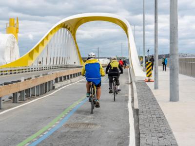 Cyclists ride in a separated bike lane through a yellow and white arched bridge.
