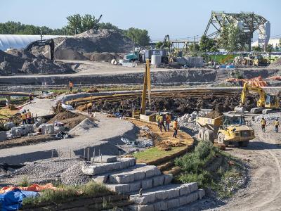 The bank of a new river curves through an excavated area. There is no water in the river yet.