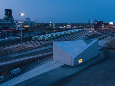 Aerial photo of an angular building at dusk with a railyard in the background.