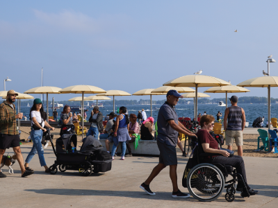 People at a beach on a summer day. One person is using a wheelchair, another is pushing a stroller. 