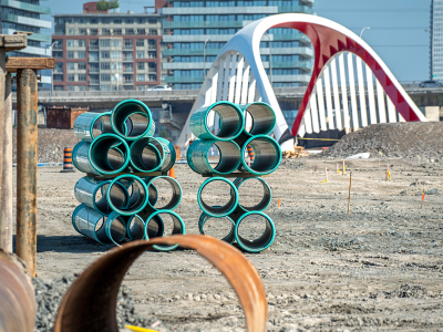 Blue pipes stacked in front of a bridge in a construction site.