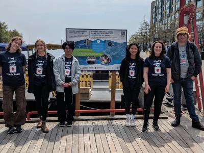 Group of six individuals wearing "U of T Trash Team" T-shirts standing in front of a board about water ecosystems.
