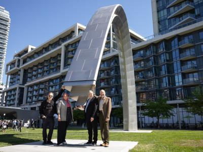 Four people pose next to a large arch - public art installation at the official unveiling in Sherbourne Common.
