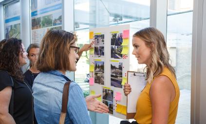 people standing and talking next to public meeting display boards