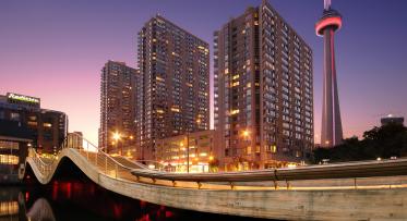 photo shows the curves and red underlighting of the Simcoe WaveDeck at dusk with buildings and the CN Tower in the background