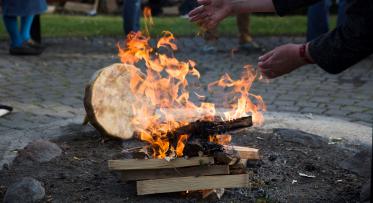 Two hands tending to a fire. A Hyde drum is behind the fire. 